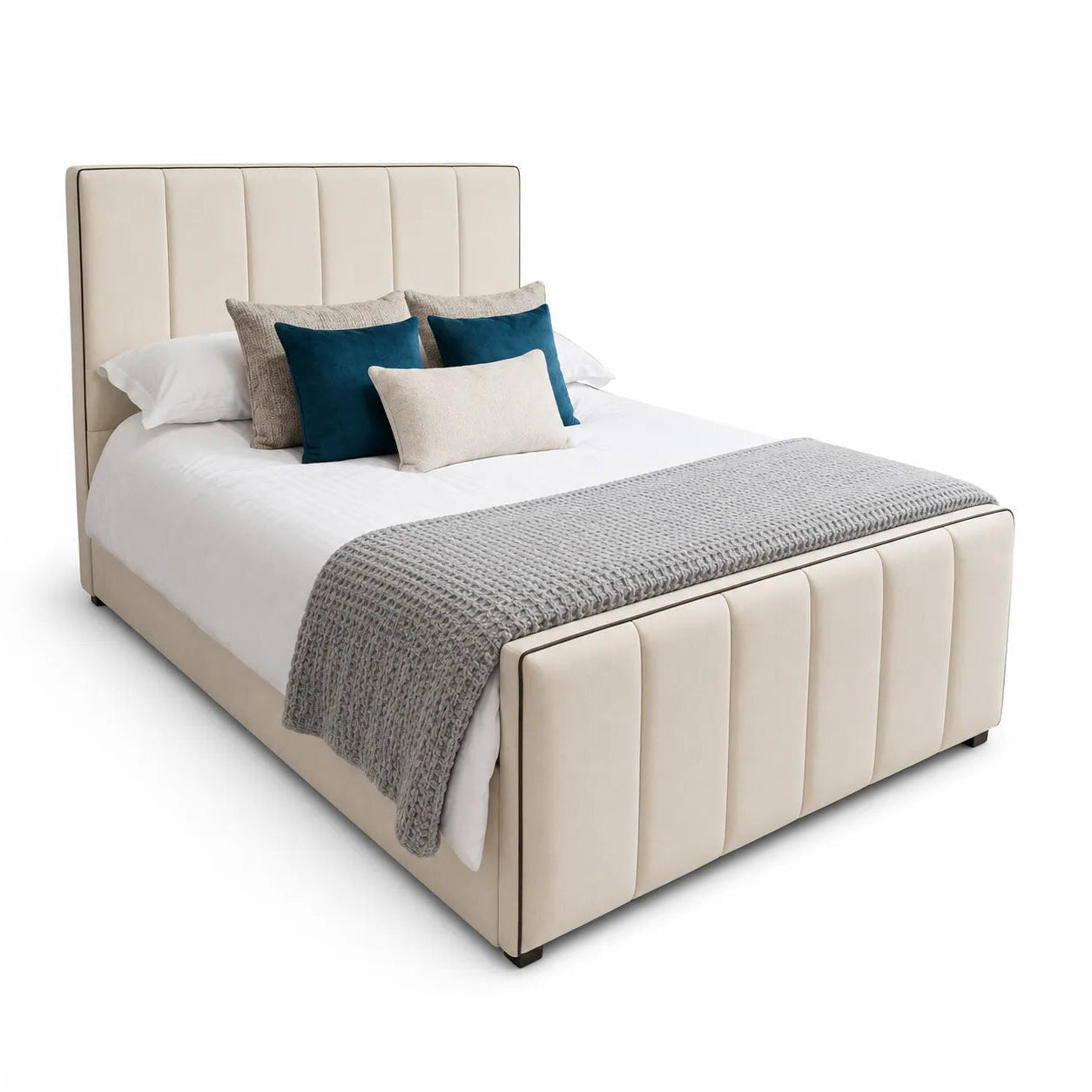 A modern platform bed with a tall, vertically channel-tufted upholstered headboard and matching footboard in a warm cream or beige fabric. The bed is styled with white bedding, a textured gray knit throw blanket, and several accent pillows in teal and light beige, set against a plain white studio background.